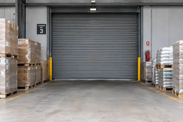 A warehouse loading bay with pallets stacked against a closed shutter.